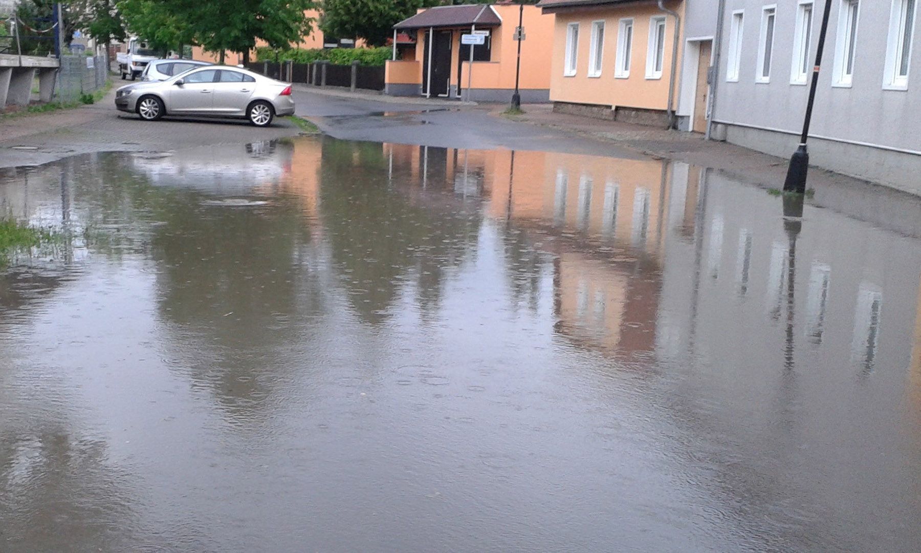 überflutete Straße mit Auto und Häusern im Hintergrund