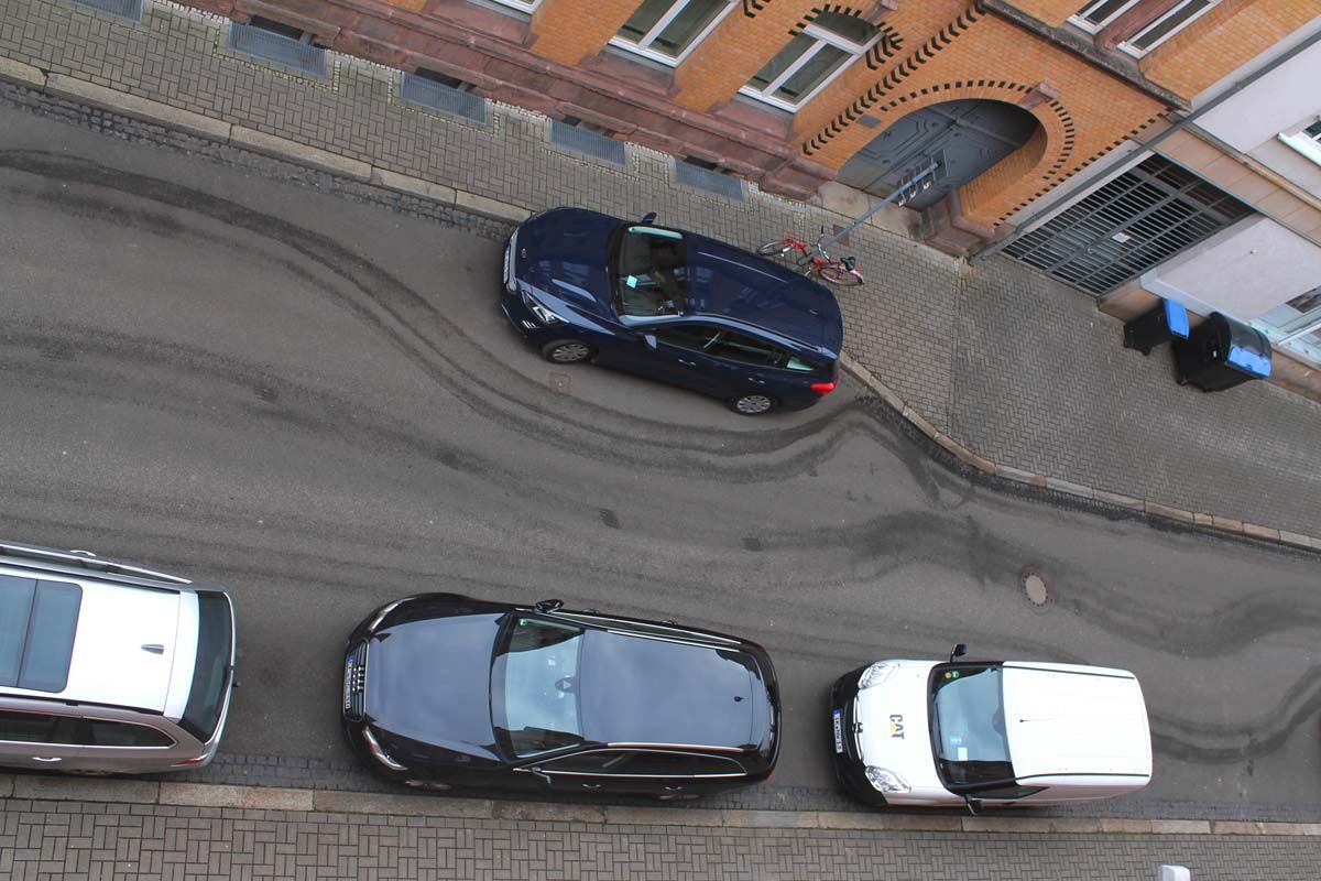 parkende Autos auf Straße mit Spuren der Straßenkehrmaschine