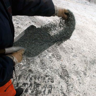 Mann verteilt Winterstreugut auf verschneiter Straße
