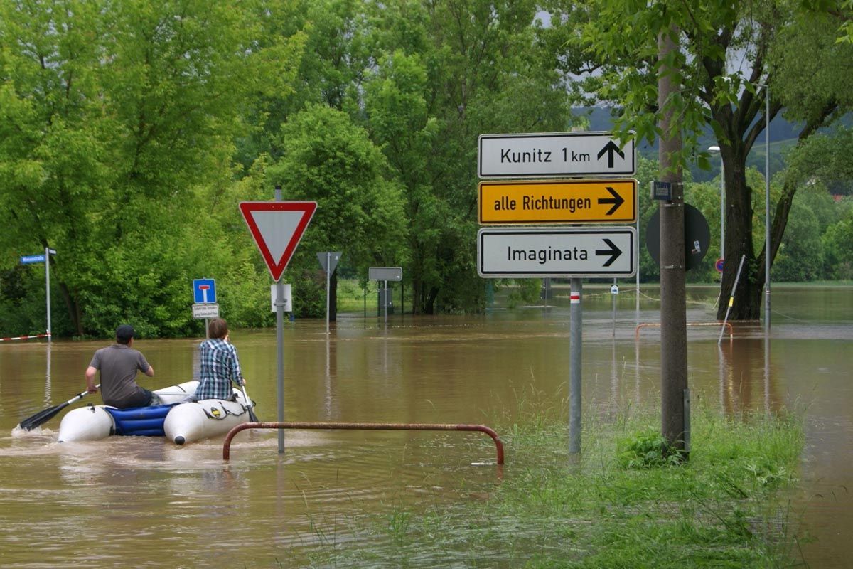 überschwemmte Straße, Schlauchboot mit 2 Personen, Straßenschild